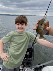 A young angler proudly displaying a Bluegill while fishing on a calm lake, showcasing a joyful moment on the water.