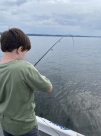 A young angler is actively reeling in a fish while fishing on a calm lake, showcasing the excitement of the catch.