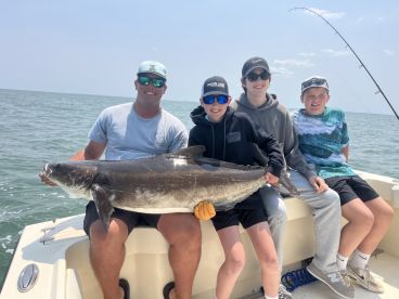 A family enjoying a successful fishing trip, showcasing a large Cobia caught in open waters.