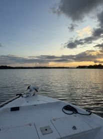 A serene view from the front of a boat at sunset, showcasing calm waters and a picturesque sky, ideal for a relaxing fishing trip.