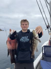A young angler proudly displaying a large Rockfish and a Bass while fishing off the coast, showcasing a successful day on the water.