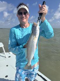 An angler proudly displaying a Speckled Trout while fishing on a boat in a coastal environment.