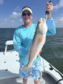 An angler proudly displaying a large Redfish while fishing on a boat in a coastal environment.