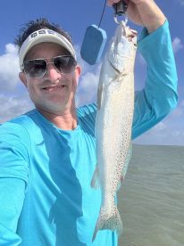 An angler proudly displaying a Speckled Trout while fishing in a coastal environment.