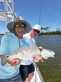 Two anglers proudly displaying a Speckled Trout while fishing on a sunny day in a coastal waterway.