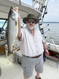 An angler proudly displaying a large Lake Trout while aboard a fishing boat, showcasing a successful day on the water.