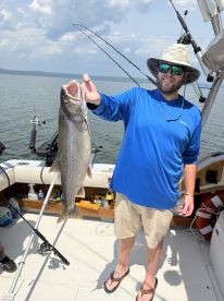 Angler proudly displaying a large Lake Trout while fishing on a boat, showcasing a sunny day on the water.