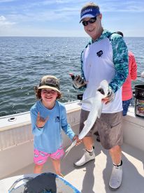 A young angler and an adult proudly displaying a caught shark while fishing on a sunny day.