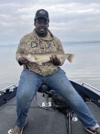 Young angler proudly displaying a Walleye while seated in a fishing boat, showcasing a calm lake environment.