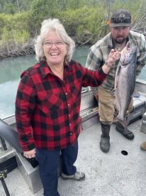 An excited angler proudly displaying a freshly caught salmon while fishing on a scenic river.