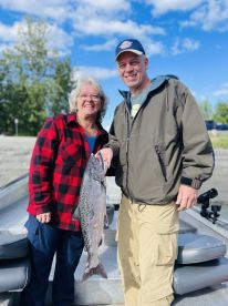 Two anglers proudly displaying a large Salmon on a fishing boat, enjoying a successful day on the water.
