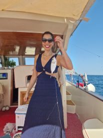 A smiling woman holding a freshly caught fish while enjoying a sunny day on a boat, showcasing the excitement of fishing in a vibrant marine environment.