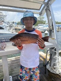 A young angler proudly displaying a Red Snapper at the marina after a successful fishing trip.