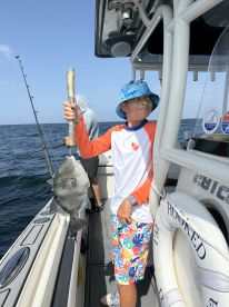 A young angler proudly displaying a Black Drum caught while fishing on a boat, showcasing a vibrant ocean backdrop.