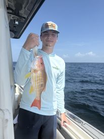 A young angler proudly displaying a colorful Snapper while fishing offshore, showcasing a sunny day on the water.