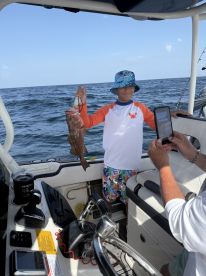 A young angler proudly displaying a caught fish aboard a boat, enjoying a day of fishing in open waters.