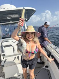 An excited angler proudly displaying a Snapper on a fishing boat, enjoying a sunny day on the water.
