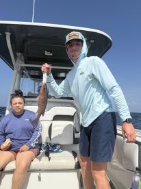 A young angler proudly displaying a Snapper while a companion enjoys a snack on the boat during a fishing trip.