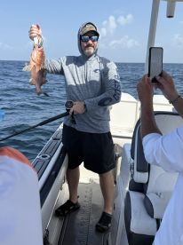 Angler proudly displaying a Red Snapper while fishing on a boat in open waters.
