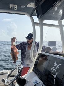 Angler holding a large Grouper while aboard a fishing boat, showcasing a successful catch during a deep-sea fishing trip.