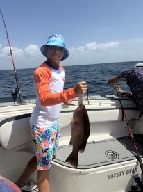 A young angler proudly displaying a large Snapper while fishing on a boat in open waters.