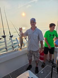 An adult angler proudly displaying a caught Walleye on a fishing boat during a sunny day, with a young boy nearby.