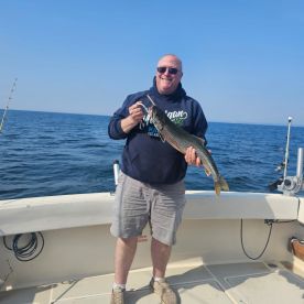 An angler proudly displaying a large Lake Trout while fishing on a boat in open waters.