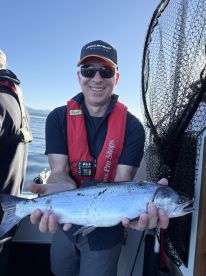 An angler proudly displaying a freshly caught Salmon while on a fishing trip, showcasing the beautiful waters in the background.