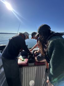 Three anglers engaged in preparing tackle on a sunny day while fishing on a boat, showcasing a collaborative fishing experience.