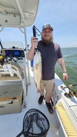 An angler proudly displaying a large Redfish aboard a fishing boat in a sunny coastal environment.
