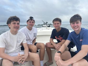 Four young anglers seated inside a boat, enjoying a day on the water, with a scenic backdrop of the coastline.