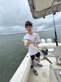 A young angler proudly displaying a caught shark while aboard a fishing boat, showcasing a cloudy day on the water.