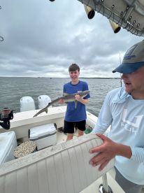 A young angler proudly displaying a caught shark aboard a fishing boat, with a cloudy backdrop on a coastal fishing trip.