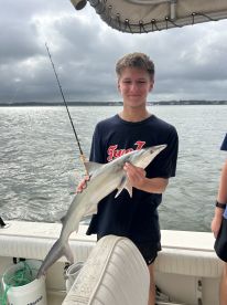 Young angler proudly holding a shark while fishing on a boat, showcasing a successful catch in a coastal environment.