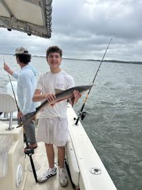 A young angler proudly displaying a caught shark while fishing on a boat, showcasing a fun day on the water.