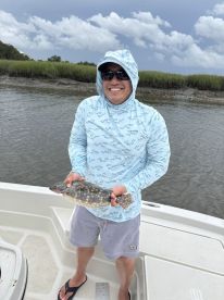 Angler proudly displaying a Flounder while fishing in a coastal environment, showcasing a sunny day on the water.