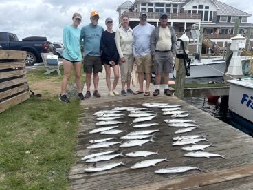 A family group poses with a successful catch of Spanish Mackerel displayed on a dock after a fishing trip.