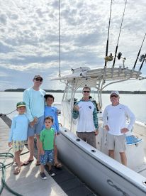 A family of five poses by their fishing boat at the dock, showcasing a beautiful day on the water.
