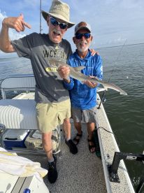 Two anglers proudly displaying a small shark caught during a fishing trip, showcasing a fun moment on the water.
