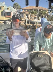 A young angler proudly displaying a caught fish while on a fishing charter, with a scenic waterfront backdrop.
