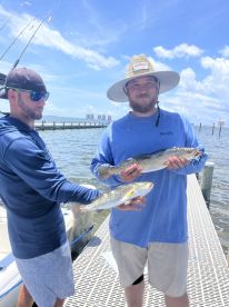 Two anglers proudly displaying their catches of Speckled Trout while docked, showcasing a successful day on the water.
