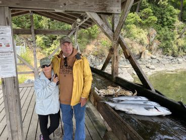 A couple stands together at a dock showcasing their catch, including several fish and crabs, after a successful fishing trip.