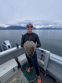 Angler proudly displaying a large Halibut while fishing in a scenic coastal environment.