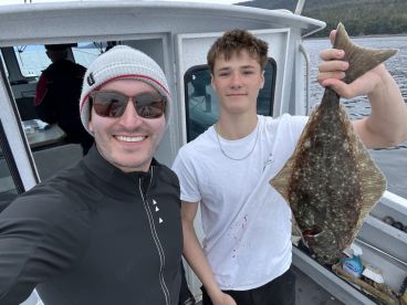 A young angler proudly displaying a large Halibut while on a fishing charter, with scenic waters in the background.