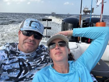 A couple enjoying a relaxing moment on a fishing boat, with offshore oil rigs visible in the background, showcasing a casual day on the water.