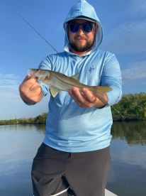 Angler proudly displaying a Snook caught during a fishing trip in a calm coastal environment.