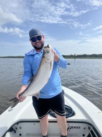 Angler proudly displaying a large Speckled Trout while fishing on a boat in a coastal waterway.