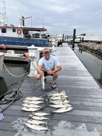 An angler proudly displaying a large fish alongside a catch of multiple Black Drum on a dock after a successful fishing trip.
