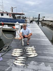 An angler proudly displaying a catch of multiple fish, including Spanish Mackerel, on the dock after a successful fishing trip.