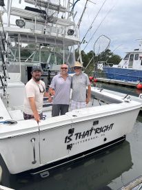 Three anglers posing on the deck of the 'Is That Right' charter boat, showcasing the boat's exterior in a marina setting.